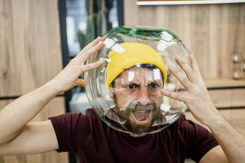 Frustrated businessman screaming while wearing fishbowl in modern office - RCPF00269