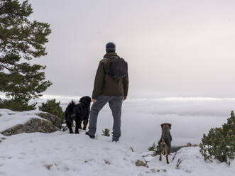 Hiker and his dog looking in the snowy mountains at foggy sky background. - ADSF05070