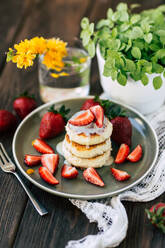 Leckere weiche Pfannkuchen mit frischen Erdbeeren auf Keramikteller neben Topfpflanze und Glas mit gelber Blume platziert - ADSF05269