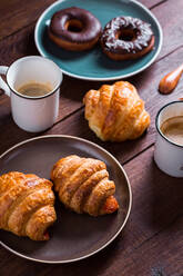 Von oben Hände einer nicht erkennbaren Person mit einer Tasse Kaffee und einem frischen Croissant. - ADSF05290