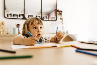 Cute girl looking away while painting on paper in dining room at home - JRFF04588