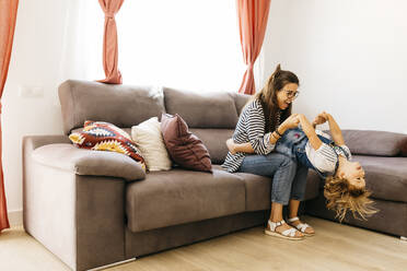 Happy mother and daughter playing on sofa at home - JRFF04598