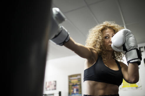 Ernste Frau trainiert im Fitnessstudio mit Boxsack - ADSF05302