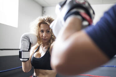 Fitness-Dame in Sportkleidung beim Sparring mit einem Mann am Ring in einer leichten Turnhalle - ADSF05303