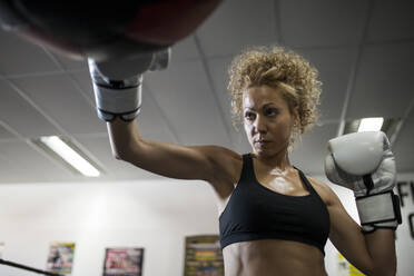 Ernste Frau trainiert im Fitnessstudio mit Boxsack - ADSF05308