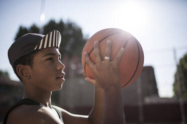 Junger Afro-Junge mit Hut spielt Basketball auf dem Platz in seiner Nachbarschaft - ADSF05373