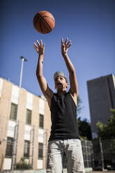 Junger Afro-Junge mit Hut spielt Basketball auf dem Platz in seiner Nachbarschaft - ADSF05383