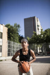 Junger Afro-Junge mit Hut spielt Basketball auf dem Platz in seiner Nachbarschaft - ADSF05385