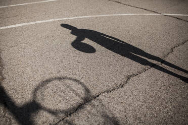 Schatten eines afroamerikanischen Jungen, der auf dem Platz in seiner Nachbarschaft Basketball spielt - ADSF05390