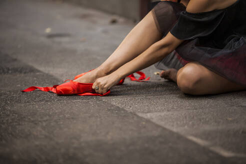 Ballerina mit rotem Kopf und schwarzem Tutu zerquetscht rote Ballettspitzen auf der Straße - ADSF05432