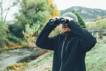 A young caucasian man with binoculars in te mountain in autumn colors - ADSF05624