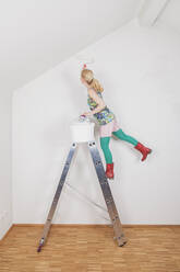 Mature woman painting wall while standing on step ladder at home - GWF06657