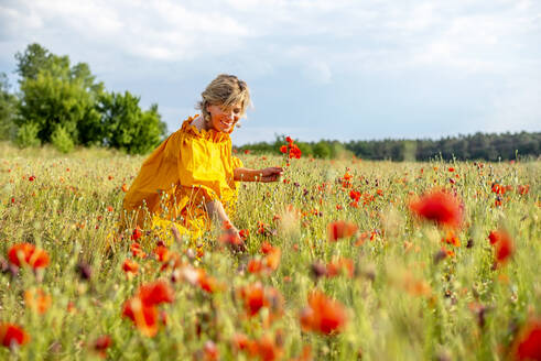 Glückliche reife Frau pflückt Mohnblumen auf einem Feld gegen den Himmel - BFRF02269