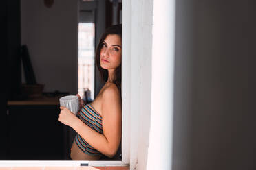 Young woman drinking coffee near window - ADSF05746