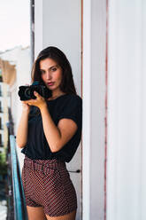 Young woman standing at balcony with photo camera - ADSF05761