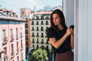 Young woman standing at balcony with photo camera - ADSF05762