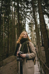 Redhead woman with camera on footbridge in woods - FSIF05082
