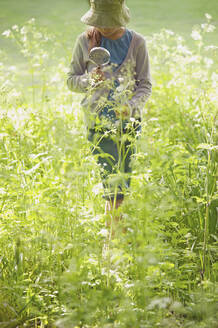 Mädchen mit Vergrößerungsglas, das Pflanzen und Blumen untersucht - FSIF05087