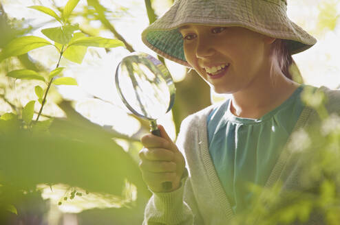 Lächelndes neugieriges Mädchen mit Vergrößerungsglas, das Pflanzen untersucht - FSIF05092
