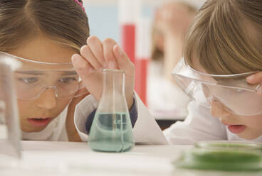 Curious junior high school girl students examining liquid in science beaker - FSIF05106