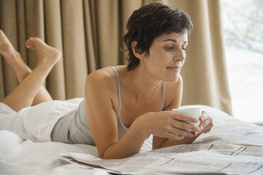 Frau entspannt sich auf dem Bett und liest Zeitung mit Kaffee - FSIF05128