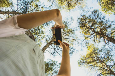 Aufgeregte junge Frau steht im Wald und macht ein Foto mit einer Retro-Kamera - ADSF05874