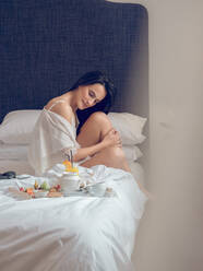 Young woman having breakfast sitting on bed - ADSF05943