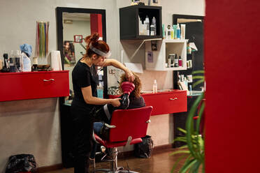 Friseurin mit Gesichtsschutz trocknet die Haare ihrer Kunden in ihrem Salon - CAVF87381