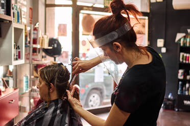 Friseur schneidet einer Kundin die Haare mit einem Gesichtsschutz - CAVF87385