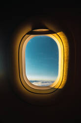 Shot aus dem Inneren des Flugzeugs Fenster mit blauen Himmel hinter beleuchtet mit goldenen Lichtern des Sonnenuntergangs - ADSF05997