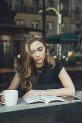 Young woman reading book in cafe - ADSF06000