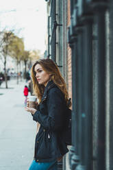 Seitenansicht einer hübschen Frau, die mit einem Pappbecher Kaffee auf der Straße steht. - ADSF06004