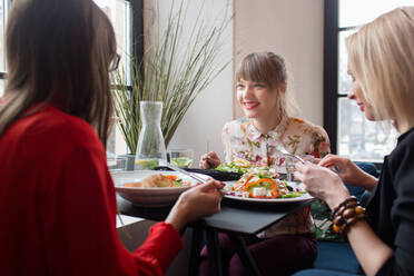 Drei junge Frauen in Freizeitkleidung unterhalten sich beim gemeinsamen Abendessen in einem hellen Restaurant. - ADSF06034