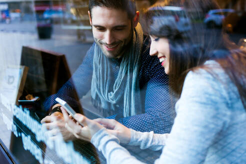 Porträt eines schönen jungen Paares, das in einem Restaurant ein Mobiltelefon benutzt. - ADSF06067