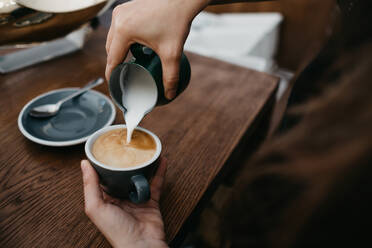 Person, die Milch in den Kaffee gießt - ADSF06086