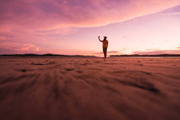 Blick in die Ferne auf einen Mann, der an einem leeren, abgelegenen Sandstrand im rosa Licht des Sonnenuntergangs steht, Bocas del Toro - ADSF06118