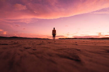 Blick in die Ferne auf einen Mann, der an einem leeren, abgelegenen Sandstrand im rosa Licht des Sonnenuntergangs steht, Bocas del Toro - ADSF06119