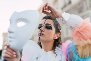 Young woman with theatrical costume and white mask while acting on street of city - ADSF06132