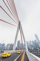 Perspective view of modern suspension bridge construction with card riding on background of metropolis of Chongqing - ADSF06147