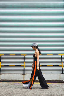 Side view of stylish young Asian woman walking at metal wall