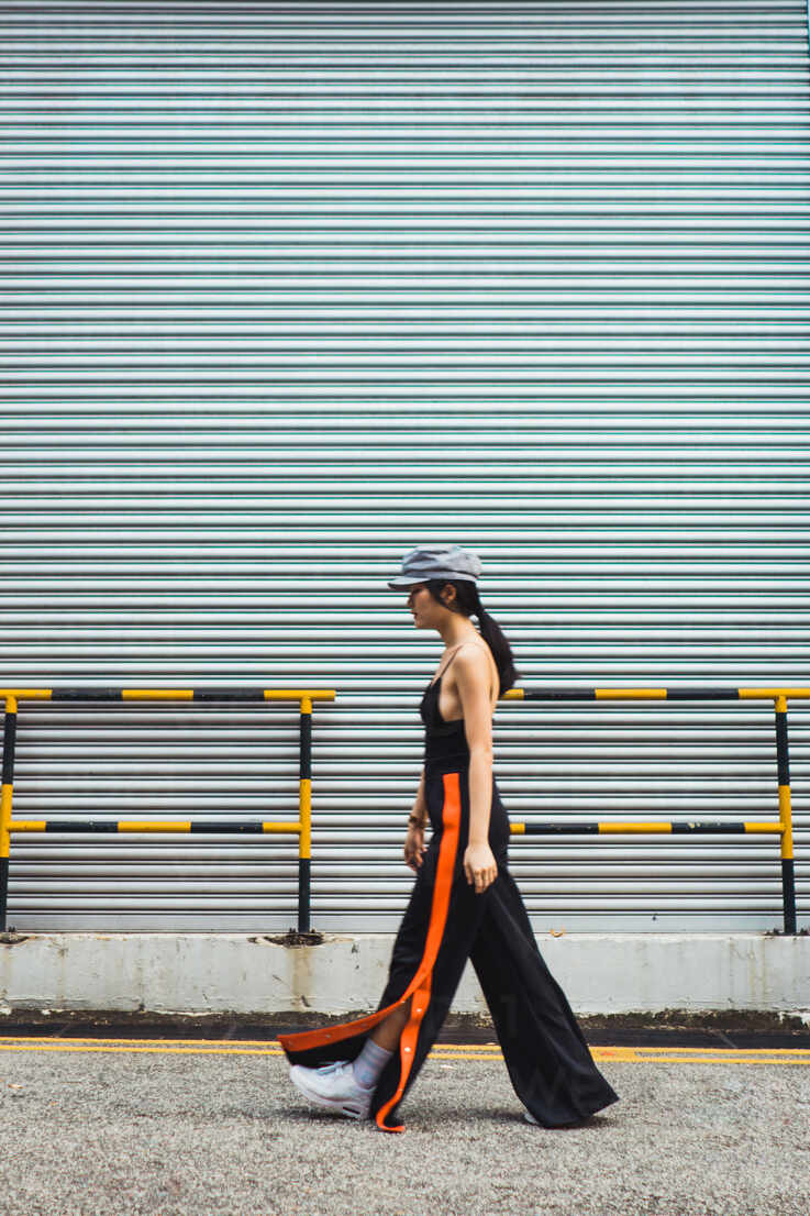 Side view of stylish young Asian woman walking at metal wall. stock photo