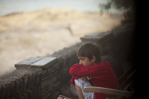 Nachdenklicher Junge sitzt an einer Felswand - CAIF28388