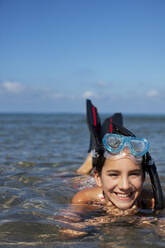 Smiling girl with snorkel and goggles laying in ocean - CAIF28400