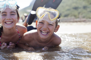 Enthusiastic brother and sister wearing goggles and laying in ocean - CAIF28401