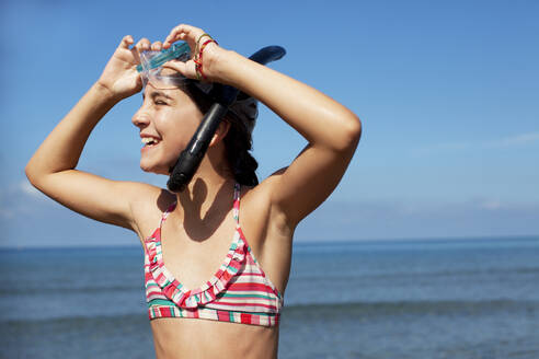 Lächelndes Mädchen mit Schnorchel und Schwimmbrille am Strand - CAIF28402