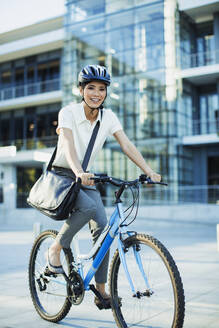 Lächelnde Frau beim Fahrradfahren auf dem Bürgersteig - CAIF28410