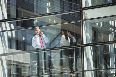 Smiling businessman talking on cell phone at window - CAIF28412