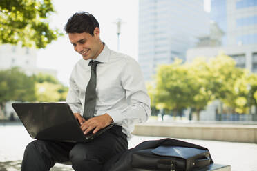 Lächelnder Geschäftsmann arbeitet an einem Laptop in einem Stadtpark - CAIF28448