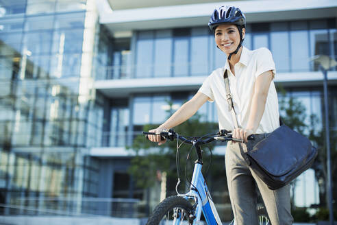 Geschäftsfrau mit Fahrrad vor städtischem Gebäude - CAIF28457