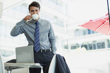 Businessman sipping coffee in office - CAIF28472
